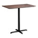 A rectangular bar height table with a textured walnut finish top and a black cross base plate.