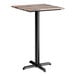 A square bar height table with a textured mixed plank finish top and a black cross base plate.