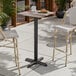 A square bar height table with a textured mixed plank finish top and a black cross base plate.