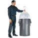 A man putting a plastic bag in a Continental gray round trash can.