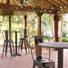 A Lancaster Table & Seating round bar height table with a cross base plate on a covered patio.