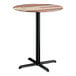 A round bar height table with a textured mixed plank finish top and a black cross base plate.