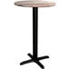 A Lancaster Table & Seating round wooden table with a black cross base.