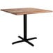 A Lancaster Table & Seating Excalibur square dining table with a Yukon oak finish and black cross base.
