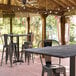 A Lancaster Table & Seating rectangular bar height table with a smooth finish and cross base plate on a covered outdoor patio with chairs.