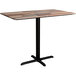 A Lancaster Table & Seating rectangular counter height table with a textured wooden top and black cross base plates.