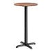 A round bar height table with a textured Yukon oak finish top and a black cross base plate.