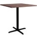 A Lancaster Table & Seating square counter height table with a textured walnut top and black cross base.