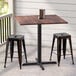 A Lancaster Table & Seating Excalibur square counter height table with a textured walnut finish and two stools on a porch.