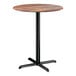 A round bar height table with a textured Yukon oak finish top and a black cross base plate.