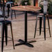 A round bar height table with a textured oak finish top and a black cross base plate.