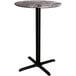 A Lancaster Table & Seating bar table with a round marble top and black cross base.