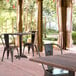 A Lancaster Table & Seating Excalibur square dining table with a textured walnut finish and cross base on a brick patio with chairs.