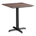 A square standard height table with a textured walnut finish top and a black cross base plate.