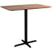 A Lancaster Table & Seating rectangular bar table with a textured Yukon Oak finish and black cross base.