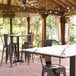 A rectangular Lancaster Table & Seating table with a white surface and black lines on a covered brick patio with black chairs.