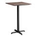 A square bar height table with a textured walnut finish top and a black cross base plate.