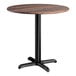 A round standard height table with a textured walnut finish top and a black cross base plate.