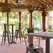 A Lancaster Table & Seating bar height table with a smooth finish on a covered patio with chairs.