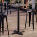 A square bar height table with a smooth dark finish and a cross base plate.