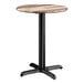 A round standard height table with a textured mixed plank finish top and a black cross base plate.