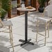 A round bar height table with a textured mixed plank finish top and a black cross base plate.