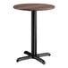 A round standard height table with a textured walnut finish top and a black cross base plate.