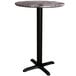 A Lancaster Table & Seating round counter height table with a black cross base.