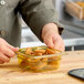 A person holding a Carlisle amber plastic food pan filled with food.