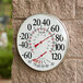 A white round Taylor wall thermometer with a hygrometer on a brick wall.