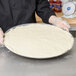 A person holding a round white dough in an American Metalcraft Super Perforated Hard Coat Anodized Aluminum Cutter Pizza Pan.