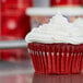 A red cupcake in a Hoffmaster white fluted baking cup.