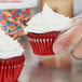 A person holding a white Hoffmaster mini baking cup with a cupcake inside.