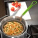 A pot of pasta in a Carlisle medium mesh culinary basket with a green handle.