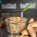 A Carlisle medium mesh fryer basket filled with french fries and a green spatula.