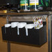 A black San Jamar cup and lid organizer with straw compartments holding white cups and lids.