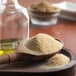 A wooden spoon filled with granulated garlic next to a glass jar of granulated garlic.