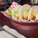 A round raspberry polypropylene server filled with tacos on a table.