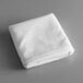 A folded white rectangular Intedge table cloth on a gray surface.