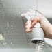 A hand holding a Unger spray gun with water droplets.