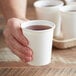 A hand holding a white Choice paper cold cup of liquid.