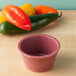 A red polyethylene ramekin on a wood surface.