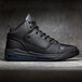 A black Shoes For Crews Tigon men's athletic shoe on a grey surface with blue soles.