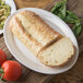 A Carlisle white oval platter with a loaf of bread on it next to tomatoes and basil.