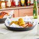 A table with two Tablecraft black plastic diner platters filled with food.