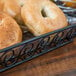 A black wrought iron rectangular basket with scrollwork holding bagels on a bakery counter.