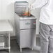 A man in a white shirt using a Main Street Equipment stainless steel floor fryer to cook food.