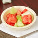 A Carlisle tan melamine nappie bowl filled with fruit on a table.