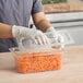 A hand in a glove places a Cambro clear plastic lid on a food container.