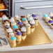 A gold laminated rectangular corrugated cake pad on a table with cupcakes on it.